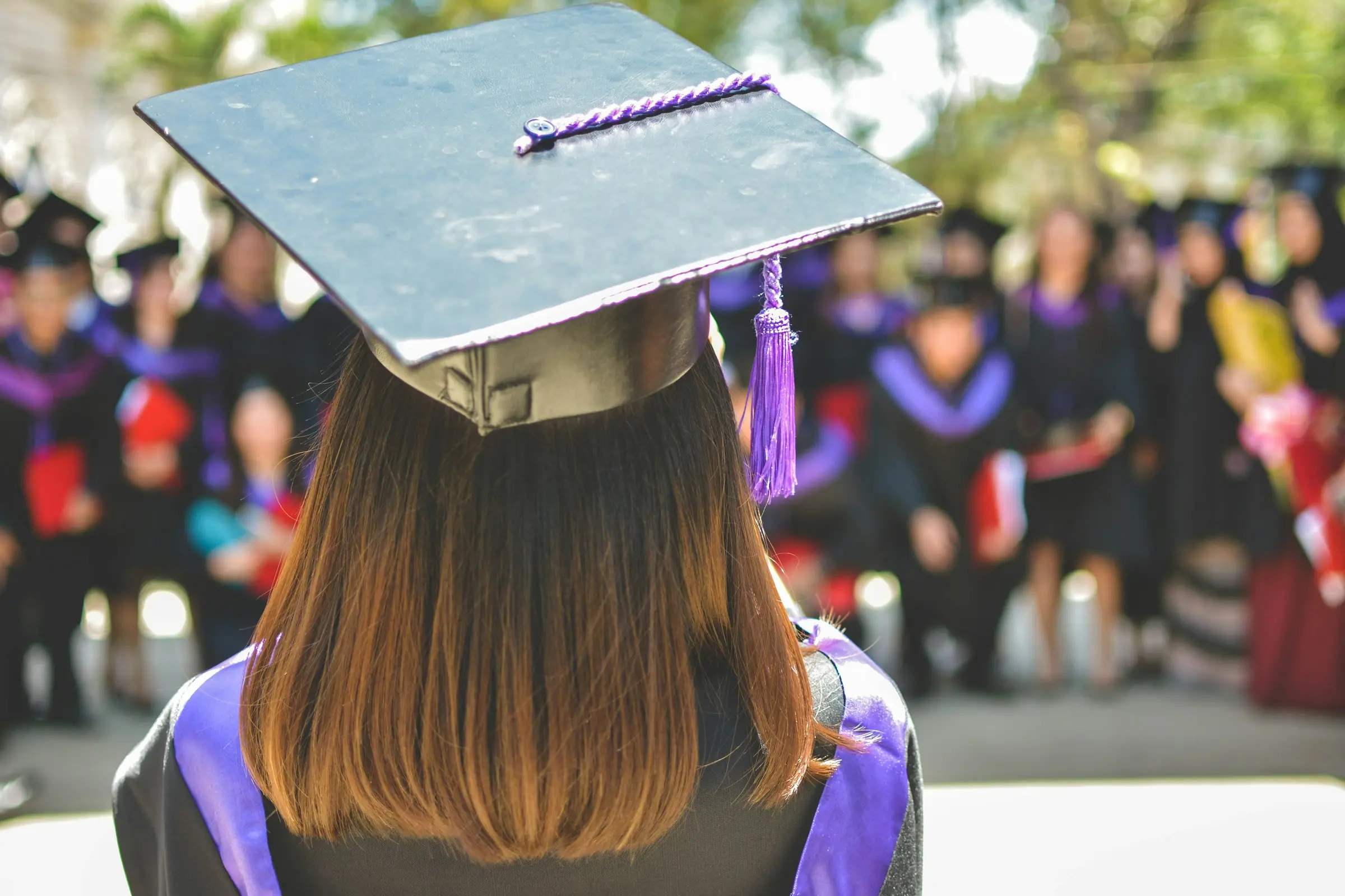 Graduate in an academic cap facing a crowd of fellow graduates
